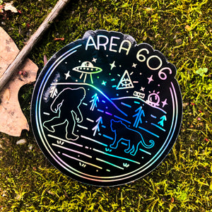 Holographic area 606 eastern kentucky conspiracy sticker. Images of bigfoot, aliens, black panther, area code 606, and black mountain. Displayed on grass.